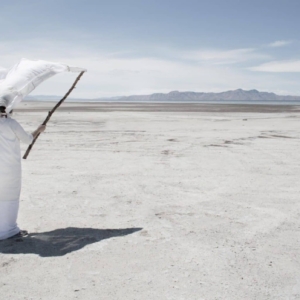 Prof. Beth Krensky walking along the salt flats dressed in a rob and headpiece attached to a stick.
